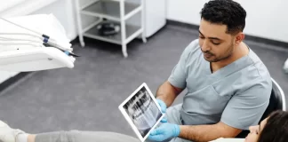 Dentysta pokazuje pacjentce zdjęcie rentgenowskie zębów na tablecie.