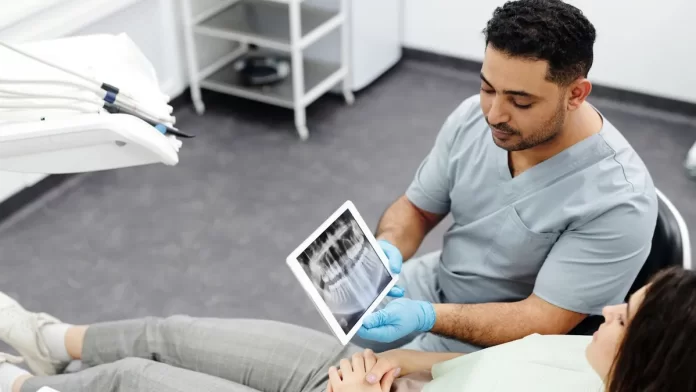 Dentysta pokazuje pacjentce zdjęcie rentgenowskie zębów na tablecie.