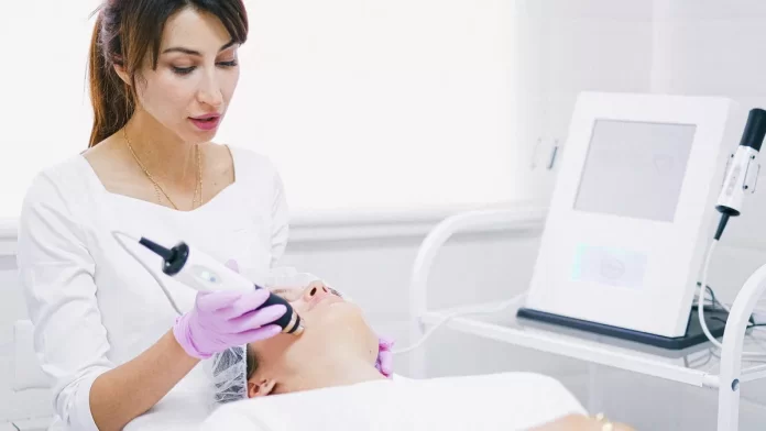 mezoterapia-beziglowa-w-gabinecie Lekarka wykonuje bezigłowy zabieg na twarzy pacjentki aparatem kosmetologicznym.